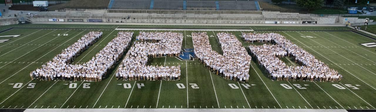 GVSU students standing on the football field in the formation of the letters GVSU.